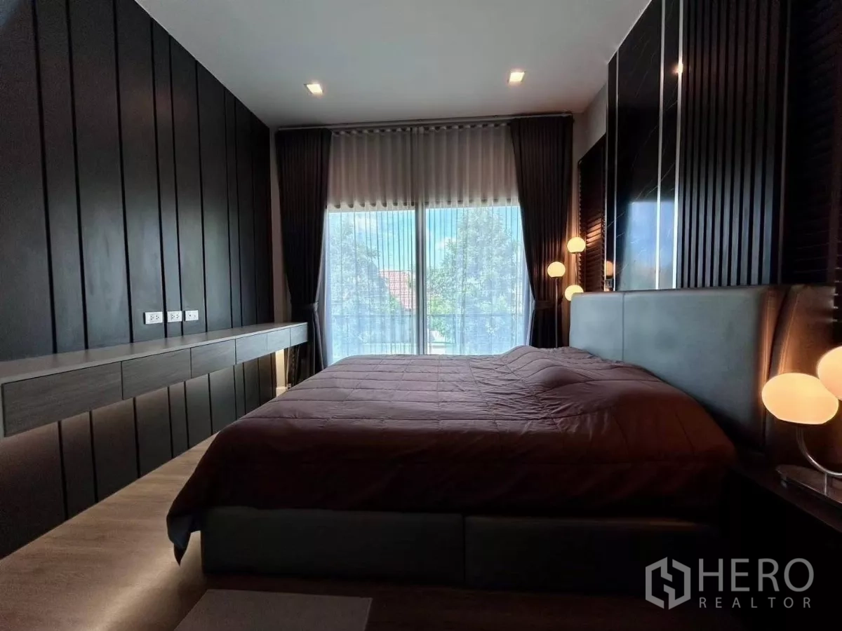 Detached House for rent in Bang Phli, Samut Prakan - Primary bedroom with dark wood paneling, large bed and full-height window to the balcony.