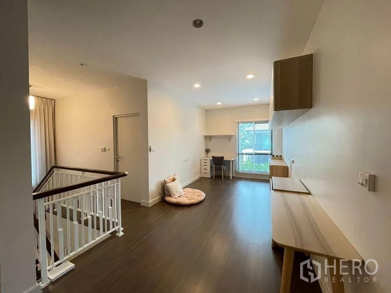 独立式住宅 出售在Pak Kret, Nonthaburi - 明亮的二层家庭区，木地板、窗边书桌与白色楼梯扶手。