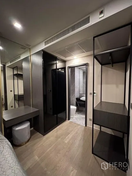 Condominium for rent in Watthana, Bangkok - Bedroom corridor with mirrored wardrobe, open shelving, vanity desk, and doorway to a marble bathroom.