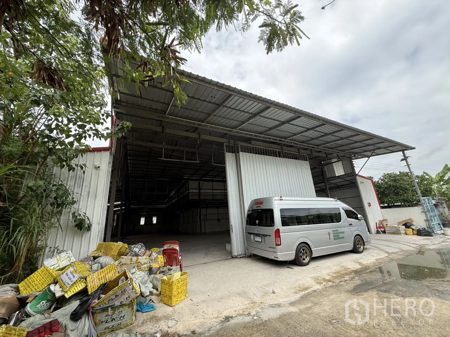 Warehouse for rent in Huai Khwang, Bangkok - Exterior of steel-frame warehouse with wide covered loading bay, open sliding doors, concrete forecourt and a parked van.
