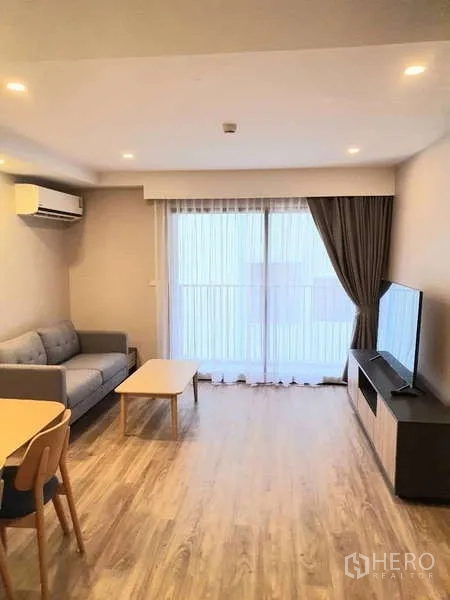 Condominium for rent in Sathon, Bangkok - Living room with sofa, TV and sliding doors to a balcony with sheer curtains.
