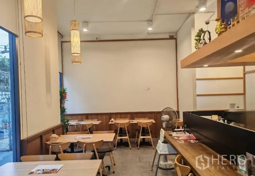 零售空间 出租在Watthana, Bangkok - 后侧座位区，吊灯与暖色木饰面，可见吧台区域。