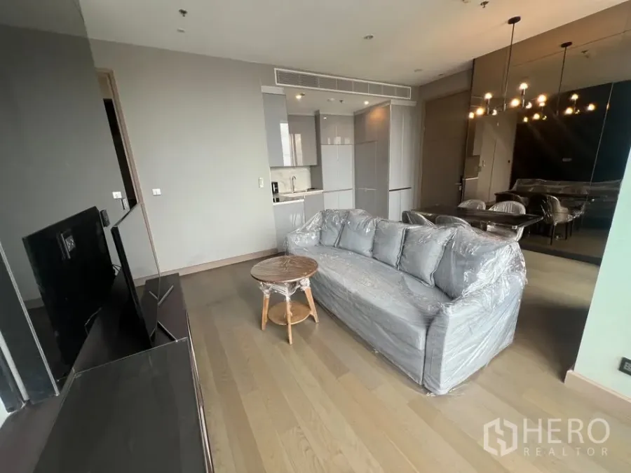 公寓 出租在Huai Khwang, Bangkok - 开放式起居区，灰色沙发、电视墙、吊灯与木地板上的小厨房。