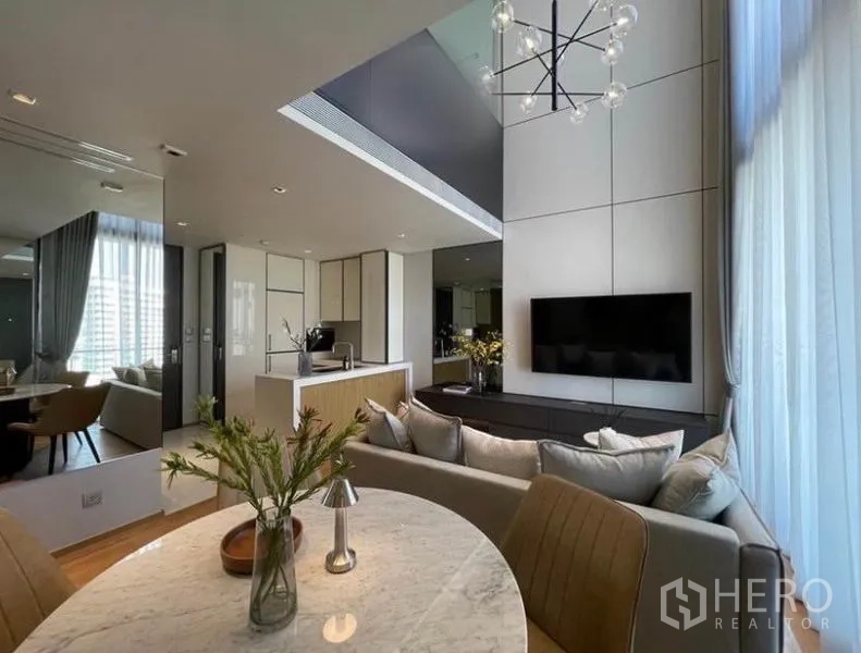 คอนโด ให้เช่าในKhlong Toei, Bangkok - มุมมองจากโต๊ะทานอาหารไปยังเคาน์เตอร์ครัวและชั้นวางทีวี พร้อมโคมไฟดีไซน์และม่านโปร่ง