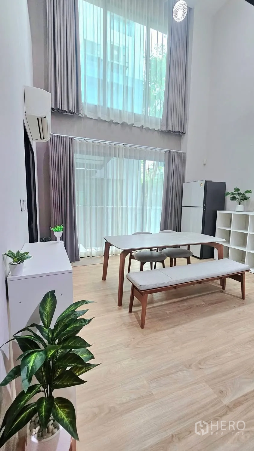Townhouse for rent in Saphan Sung, Bangkok - Dining room with tall curtains, bench seating, fridge, shelving, and indoor plants.