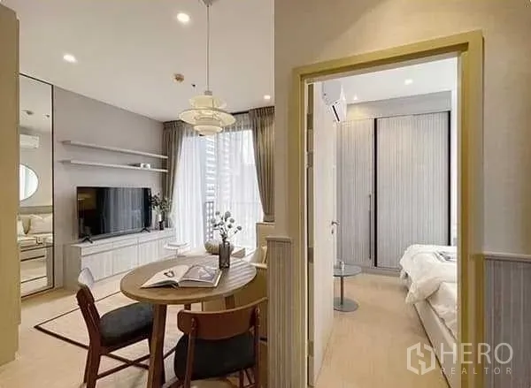 Condominium for rent in Watthana, Bangkok - Open‑plan dining and lounge with round table, TV wall unit and doorway leading to the bedroom.