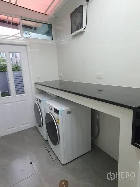 Detached House for rent - Bright laundry room with front-load washer and dryer beneath a long countertop and a side door.
