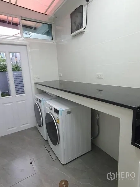 Detached House for rent - Bright laundry room with front-load washer and dryer beneath a long countertop and a side door.