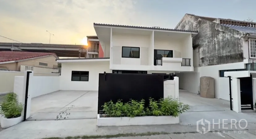 Detached House for rent in Suan Luang, Bangkok - Gated front yard with a wide driveway and parking in front of a white two-storey house.