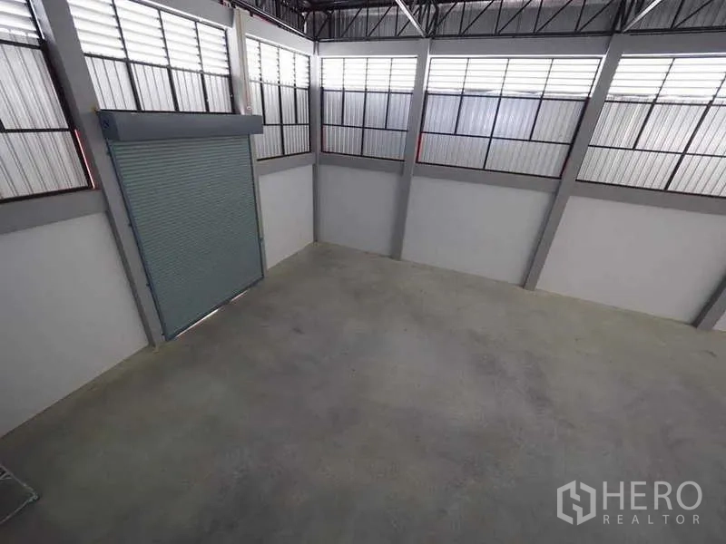 Warehouse for rent or sale in Krathum Baen, Samut Sakhon - Corner loading area with high windows and a roll-up shutter door inside the warehouse.