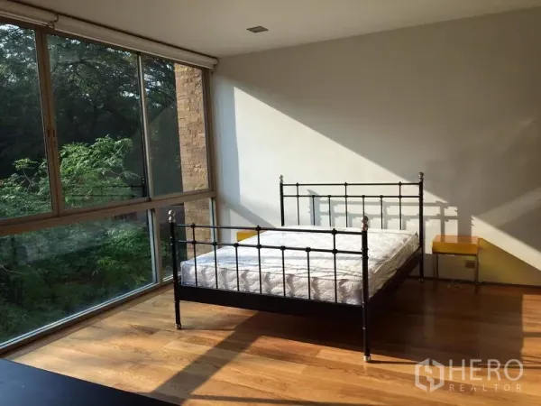 คอนโด ให้เช่าในKhlong Toei, Bangkok - ห้องนอนรับแสงธรรมชาติ เตียงเหล็ก พื้นไม้ และหน้าต่างมุมกระจกมองเห็นต้นไม้