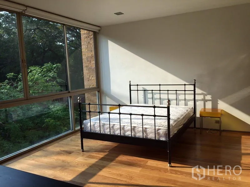 คอนโด ให้เช่าในKhlong Toei, Bangkok - ห้องนอนรับแสงธรรมชาติ เตียงเหล็ก พื้นไม้ และหน้าต่างมุมกระจกมองเห็นต้นไม้