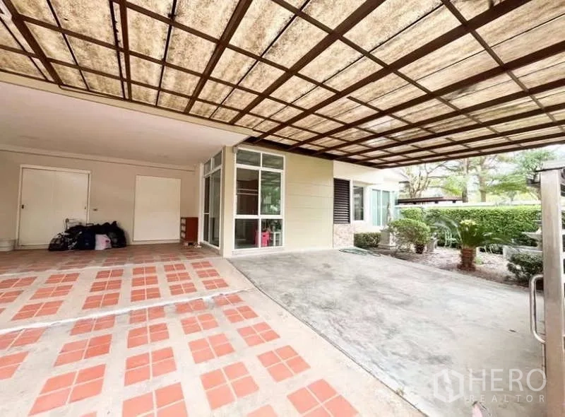 Detached House for rent in Bang Phli, Samut Prakan - Covered carport with lattice roof, tiled and concrete driveway, storage doors and trimmed garden view.