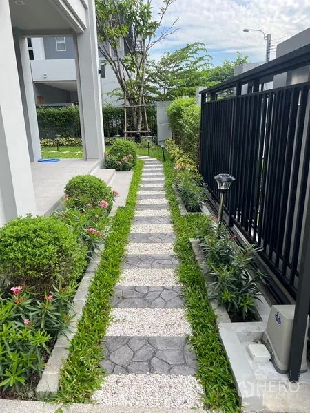 Detached House for sale in Bang Kapi, Bangkok - Front garden pathway of stepping stones bordered by trimmed hedges and a black metal fence.