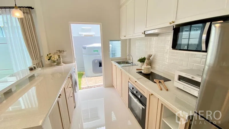 联排别墅 出租在Prawet, Bangkok - 走廊式厨房，白色橱柜、地铁砖墙面、烤箱与后门