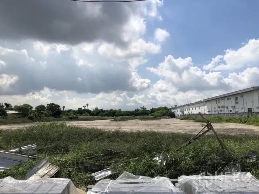 Land for sale in Mueang Pathum Thani, Pathum Thani - Leveled land parcel beside white warehouse blocks and green fields under a bright, partly cloudy sky.