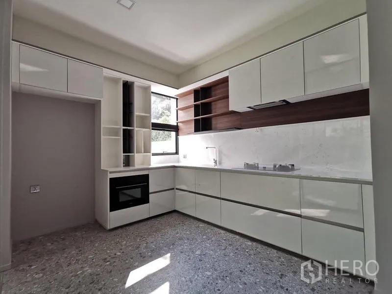 Detached House for rent or sale in Saphan Sung, Bangkok - Sleek L-shaped kitchen with glossy white cabinetry, built-in oven and a window for ventilation.