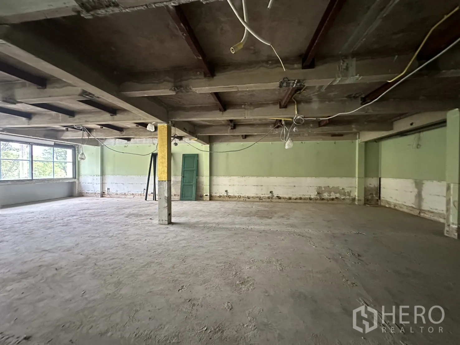 办公空间 出租在Bang Rak, Bangkok - 宽阔室内带结构柱，未完成地面与绿色墙面。