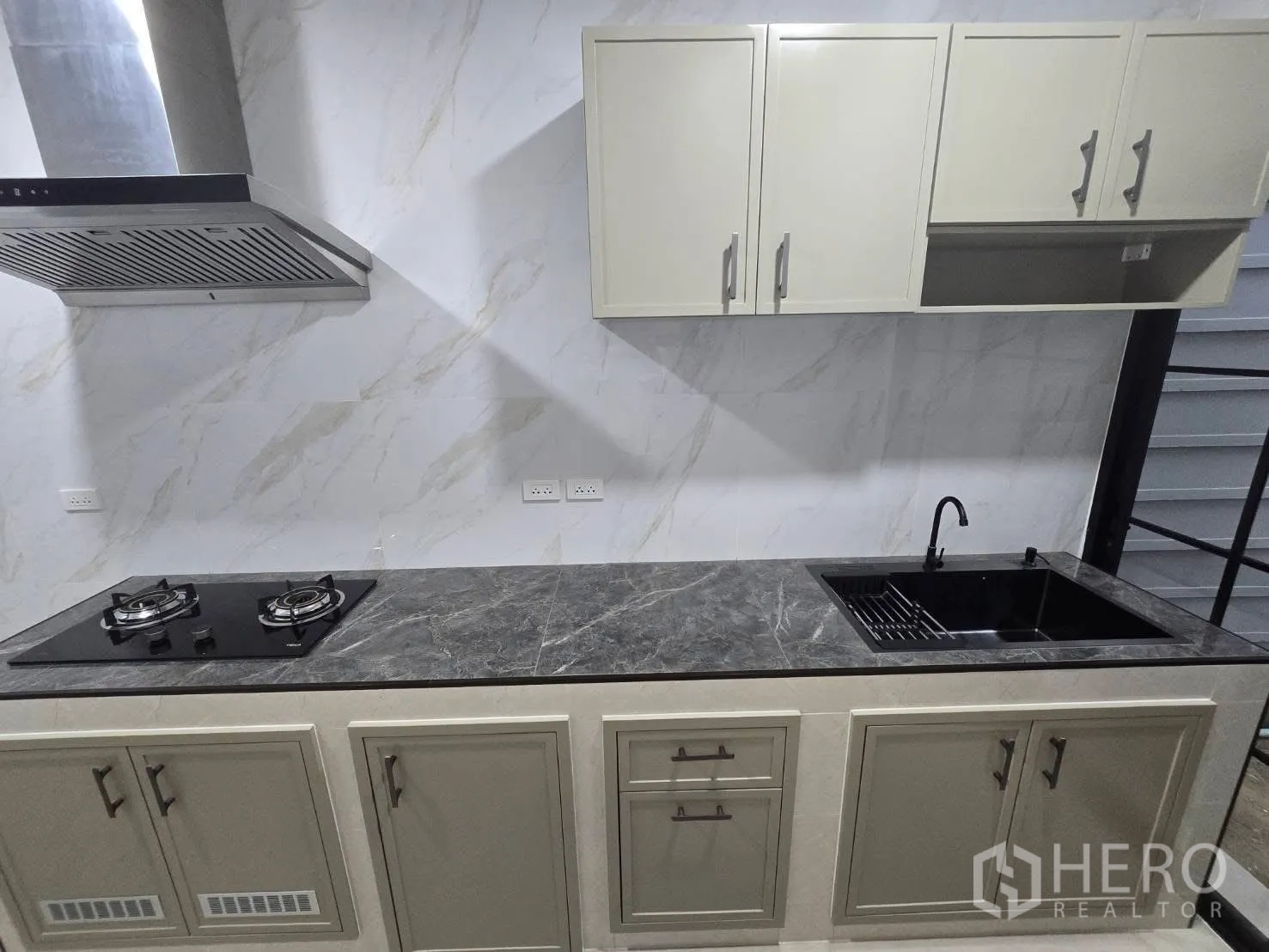 Semi-detached House for rent in Bang Phli, Samut Prakan - Kitchen cabinetry with gas cooktop, hood, and deep sink against marble-look walls.