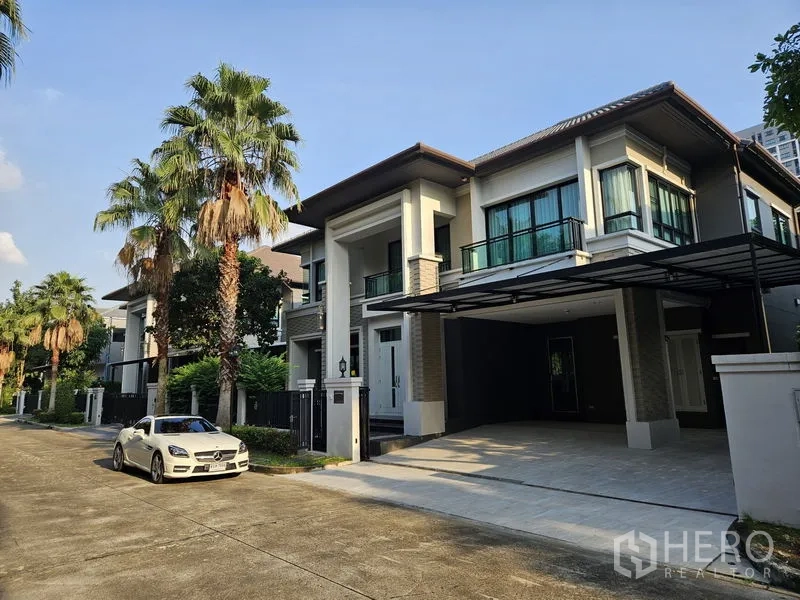 Detached House for rent in Bang Khae, Bangkok - Modern two-storey detached house with tall columns and a covered carport on a palm-lined street in Bang Khae, Bangkok.