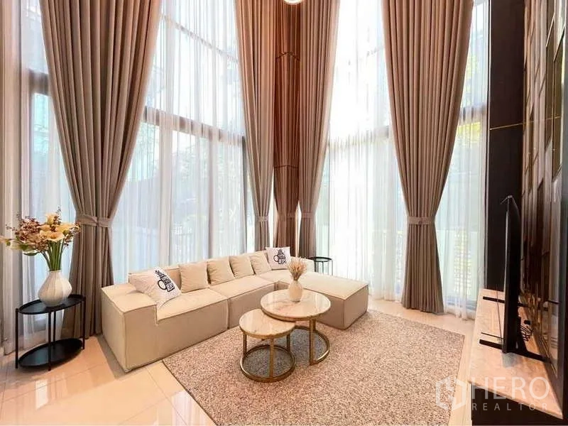 Detached House for rent in Bang Sue, Bangkok - Double-height living room with tall curtains, L-shaped sofa and TV wall.