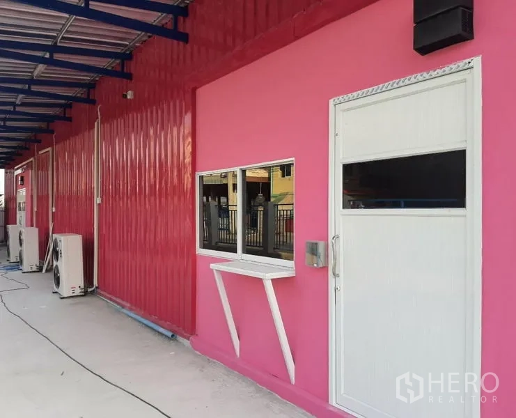 Warehouse for rent in Khlong Luang, Pathum Thani - Pink warehouse exterior with white door, sliding window, awning and AC units.
