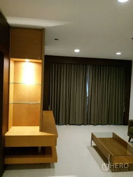 Condominium for rent in Sathon, Bangkok - Living area with built-in display shelves, floor-to-ceiling curtains, and low coffee table.