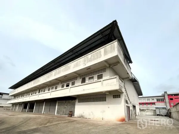 Warehouse for rent in Bang Khun Thian, Bangkok - Angled view of a multi-storey warehouse with extended metal roof and multiple loading bays in Bang Khun Thian.