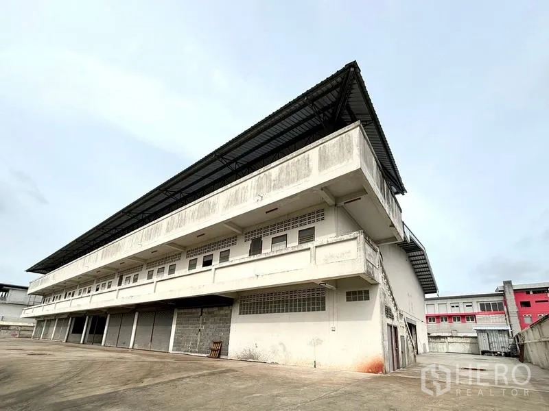 Warehouse for rent in Bang Khun Thian, Bangkok - Angled view of a multi-storey warehouse with extended metal roof and multiple loading bays in Bang Khun Thian.