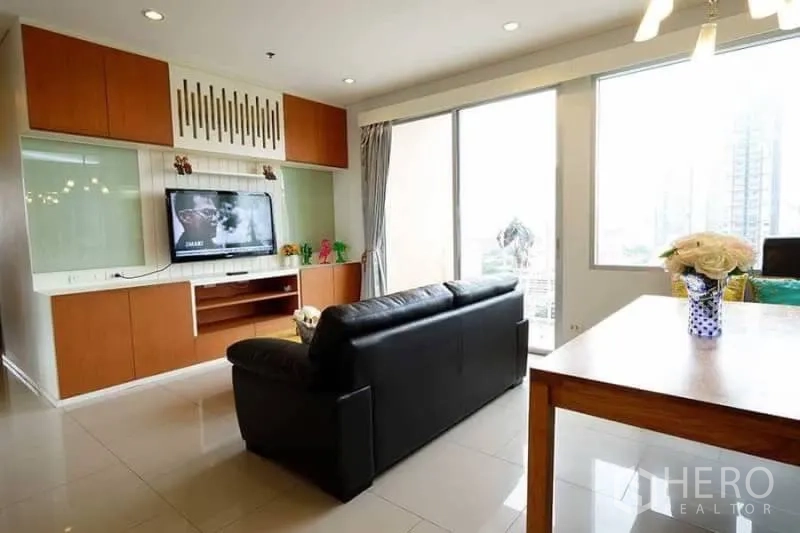 คอนโด ให้เช่าในKhlong San, Bangkok - ห้องนั่งเล่นมีผนังบิลท์อินวางทีวี โซฟาหนังสีดำ และหน้าต่างบานใหญ่เห็นวิวเมือง