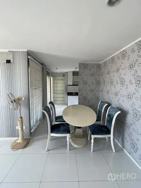 Condominium for sale in Suan Luang, Bangkok - Dining nook with round white table, upholstered chairs and floral feature wall beside the kitchen.