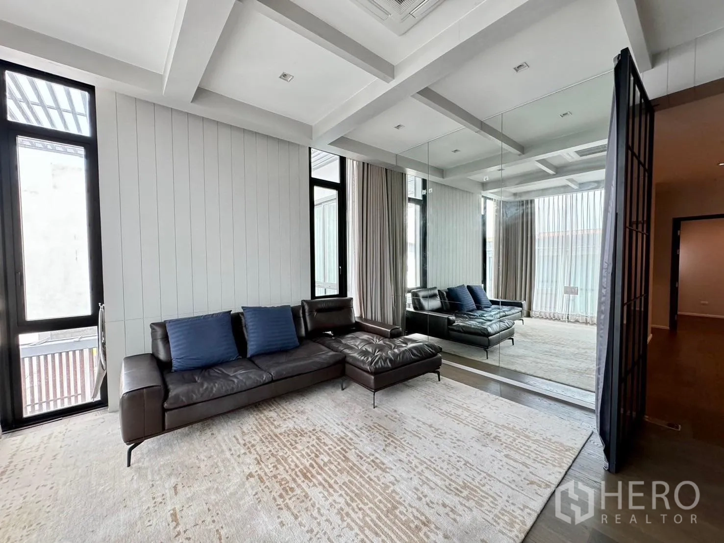 Detached House for rent or sale in Prawet, Bangkok - Lounge with leather sectional, mirrored wall and tall windows.