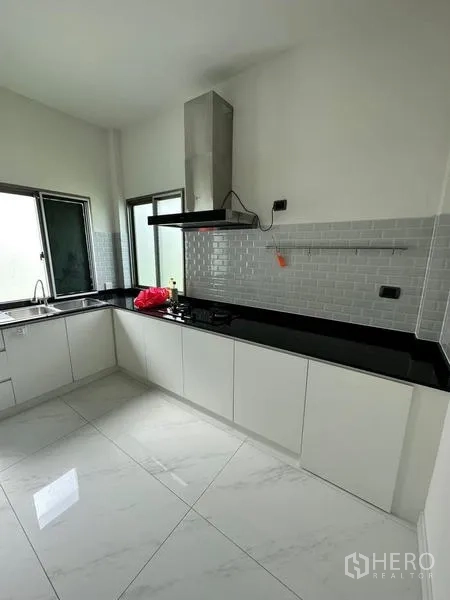 Detached House for rent in Bang Phli, Samut Prakan - Clean white kitchen with black granite countertops, subway tile backsplash, cooker hood and double windows.
