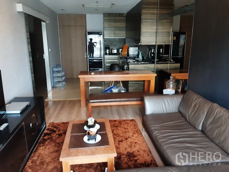 Condominium for rent in Bangkok - Open-plan lounge facing a modern kitchenette with wood cabinets, dining counter and mirrored wall.