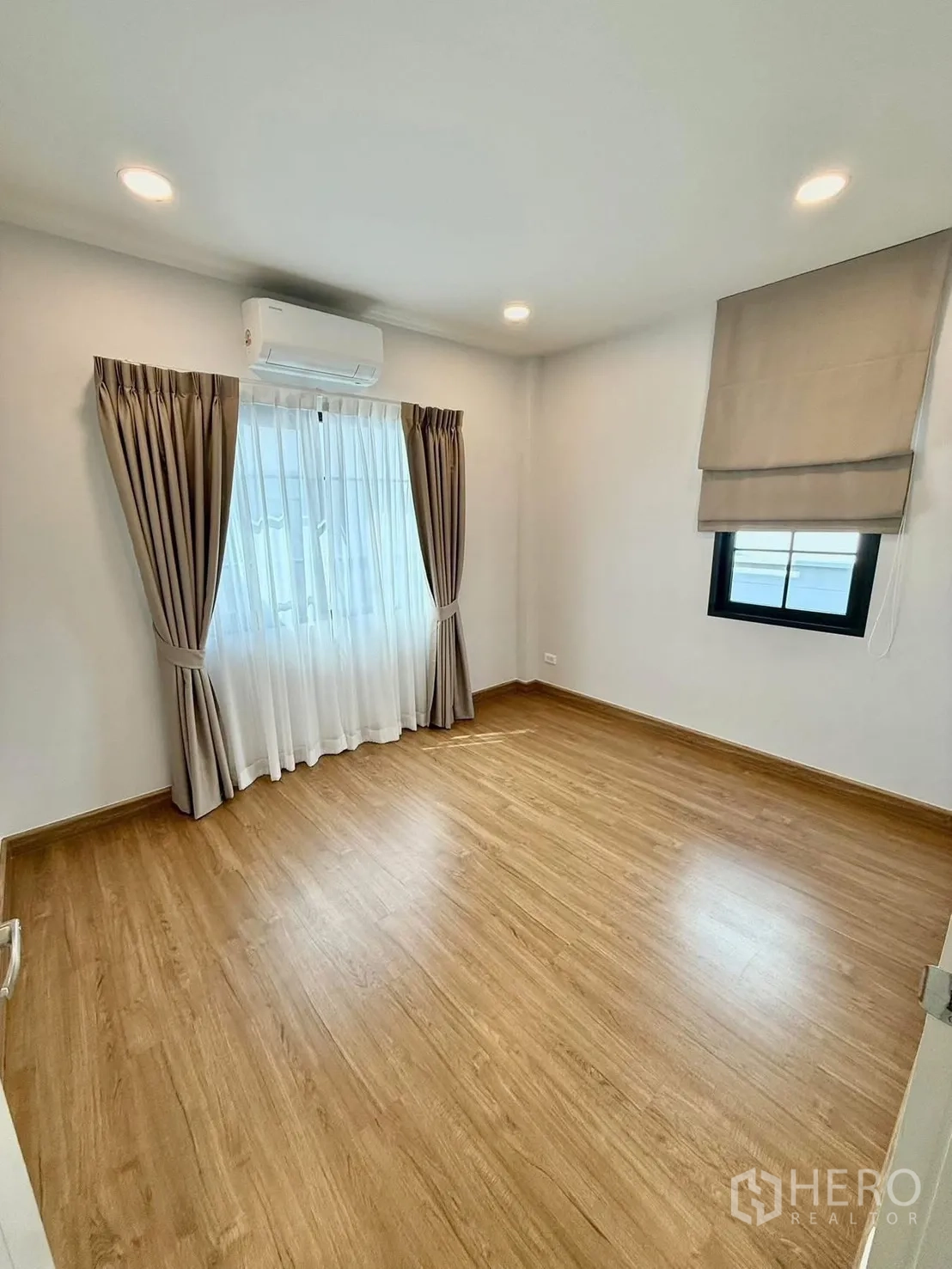 Detached House for rent in Bang Phli, Samut Prakan - Bright empty bedroom with wood floors, two windows and an air conditioner.