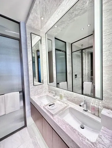 Condominium for rent - Luxurious bathroom with marble walls, double vanity sinks, and framed mirrors.