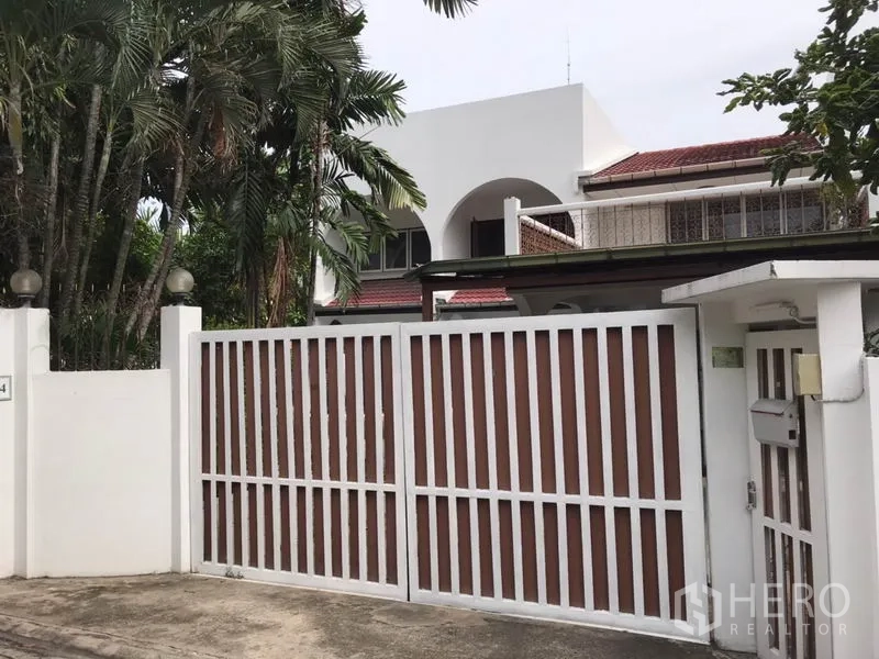 บ้าน ให้เช่าในPhra Khanong, Bangkok - บ้านเดี่ยวสองชั้นสีขาวหลังคากระเบื้องแดง พร้อมรั้วบานใหญ่และต้นปาล์มร่มรื่นในย่านพระโขนง