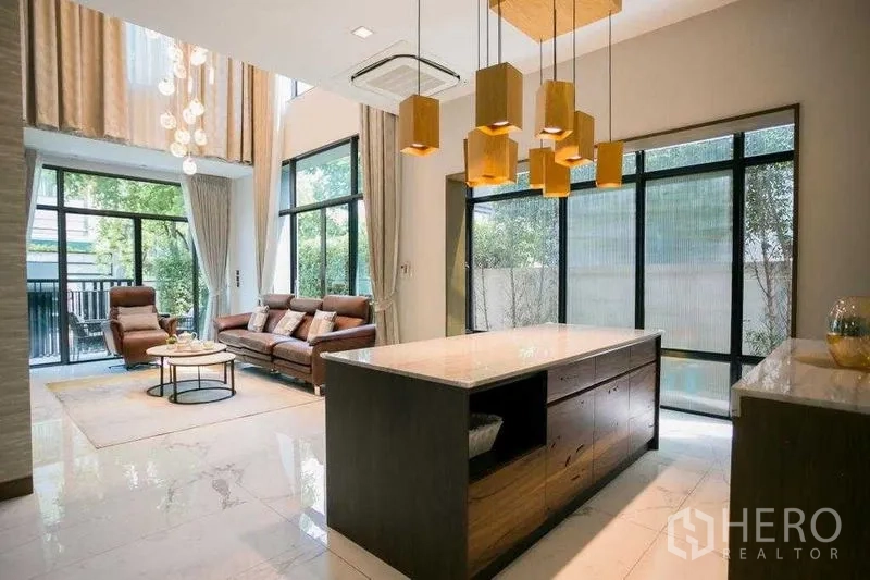 Detached House for rent in Bangkok - Open-plan living with double-height ceiling, floor-to-ceiling glass and an island kitchen with pendant lights.