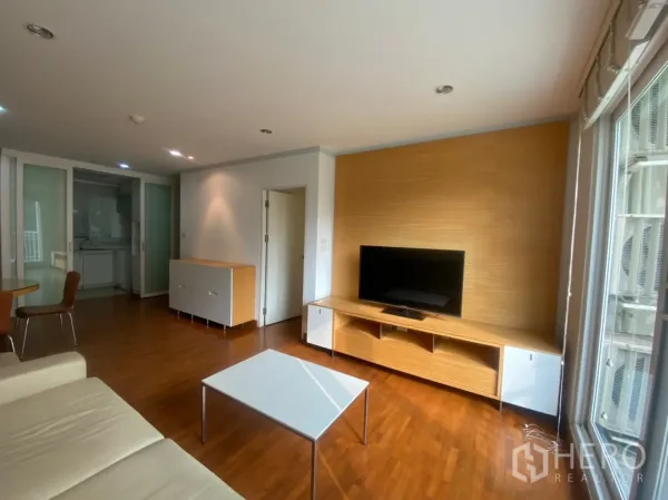 Condominium for rent or sale in Sathon, Bangkok - Bright living room with wood floors, TV console and sliding doors to a separate kitchen.