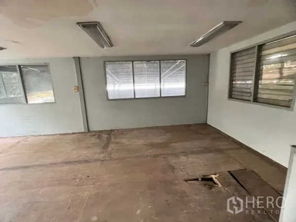 Warehouse for rent in Suan Luang, Bangkok - Secondary office area with multiple windows and worn wooden flooring inside the warehouse.