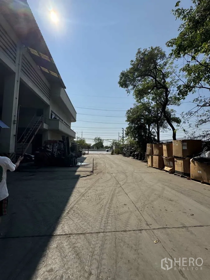 工厂 出租在Lat Lum Kaeo, Pathum Thani - 宽阔混凝土车道通向大门，两侧有树与箱件