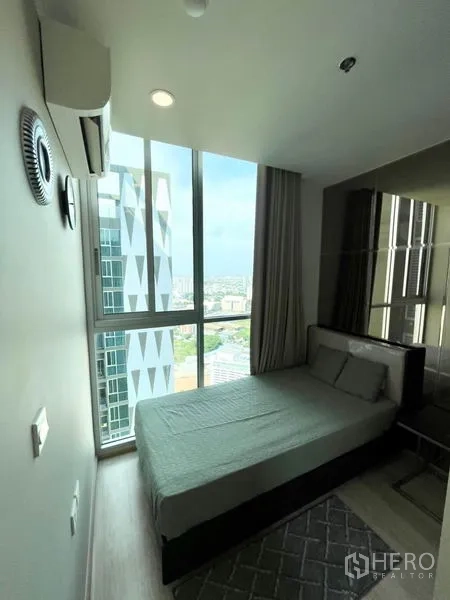Condominium for rent in Huai Khwang, Bangkok - Compact bedroom with floor-to-ceiling windows and city view beside a modern tower.
