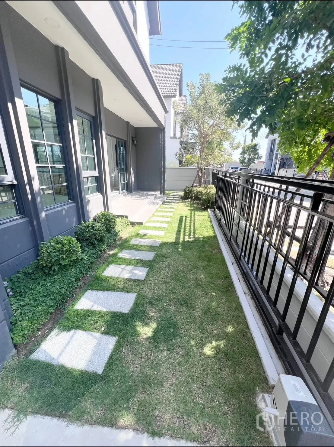 Detached House for rent in Bang Phli, Samut Prakan - Front garden strip with stepping-stone path, shrubs and metal fence along the facade.