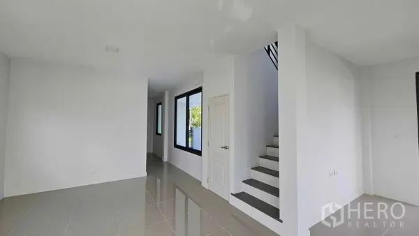 Detached House for sale in Samut Prakan - Open-plan ground floor living space with glossy tiles, staircase, and large black-framed windows.