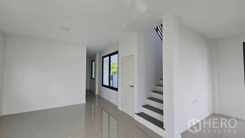 Detached House for sale in Samut Prakan - Open-plan ground floor living space with glossy tiles, staircase, and large black-framed windows.