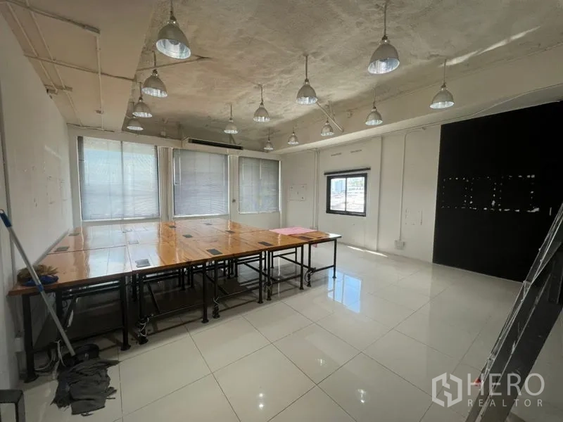 办公空间 出租在Khlong Toei, Bangkok - 采光良好的角落办公室，窗户带百叶，吊灯与木桌，配黑色特色墙。