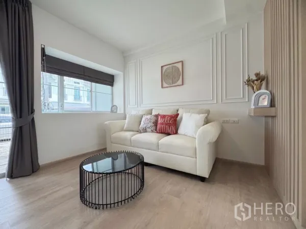 联排别墅 出租在Prawet, Bangkok - 客厅配大窗与窗帘，摆放沙发和茶几。