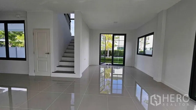 Detached House for sale in Samut Prakan - Spacious living and dining area with sliding glass doors to the garden and central staircase.
