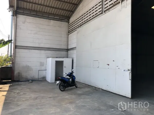 货栈 出租在Khlong Luang, Pathum Thani - 侧面装卸区，金属大门、混凝土场地及一间小型设备房。