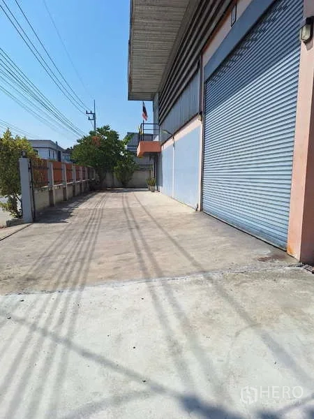 Warehouse for sale in Pathum Thani - Wide concrete loading apron in front of the warehouse with multiple blue roller shutters.